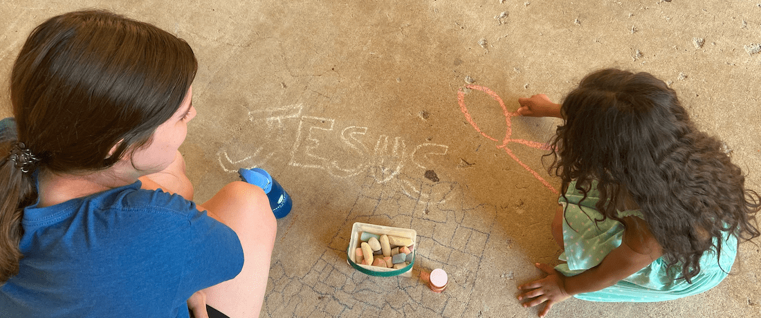 Young Girl writing "Jesus" in sidewalk chalk